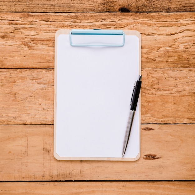 Blank paper on clipboard with ballpoint pen over wooden desk