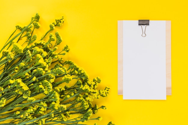 Free photo blank paper on clipboard with bunch of flowers against yellow backdrop