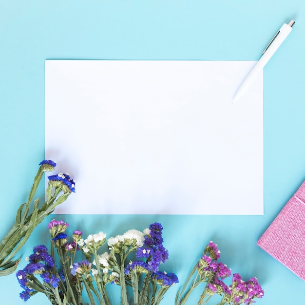 Free photo blank paper sheet; pen and bunch of colorful flowers on blue backdrop