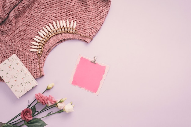 Blank paper with rose flowers, necklace and sweater on table