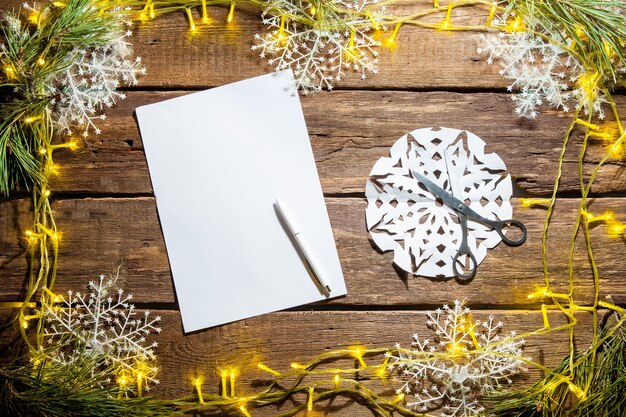 The blank sheet of paper on the wooden table with a pen and Christmas decorations.