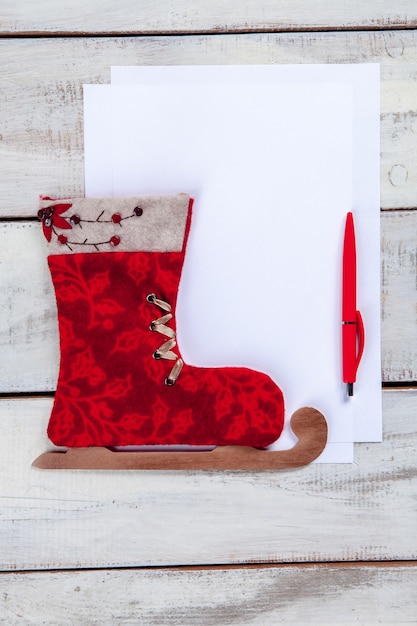 The blank sheet of paper on the wooden table with a pen and Christmas toy.