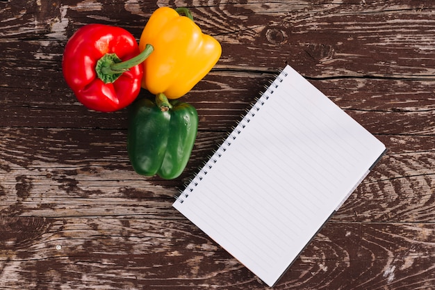 Blank single line spiral notepad with red; yellow and green bell peppers on wooden texture backdrop