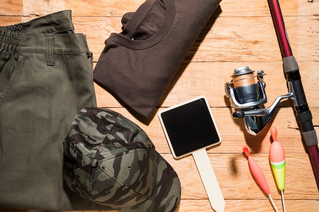 Free photo blank small placard; fishing floats; fishing rod and male clothing on wooden desk