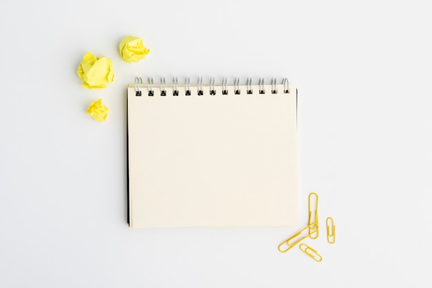 Free Photo blank spiral diary with yellow crumpled paper and paperclip over white background