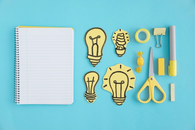 Free Photo blank spiral notebook with paper light bulbs and stationery on blue background