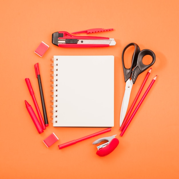 Blank spiral notepad and scissor with stationery over bright orange background