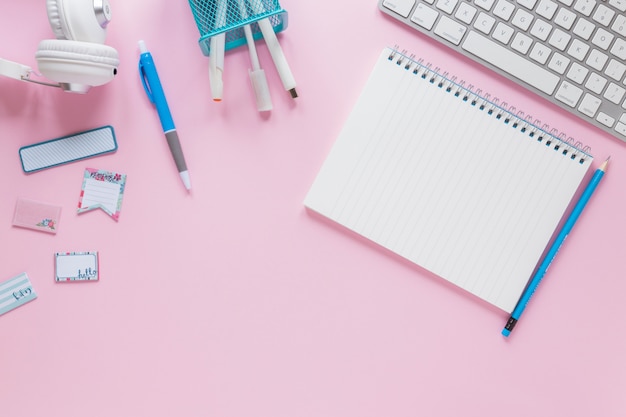 Blank spiral notepad with stationeries and keyboard on pink background