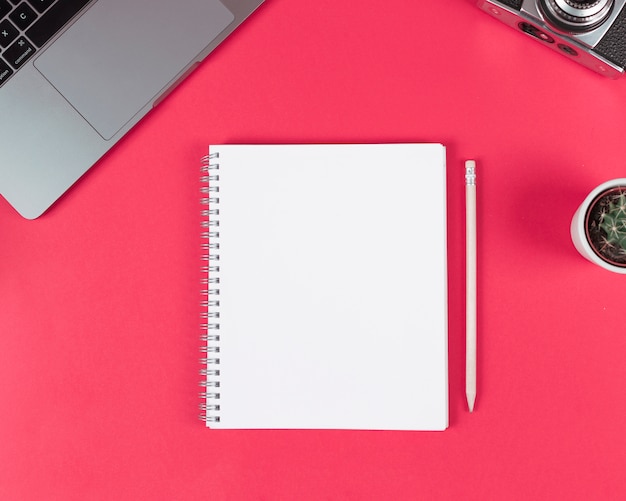 Blank spiral notepad with wooden pencil; laptop; camera and cactus plant on bright background