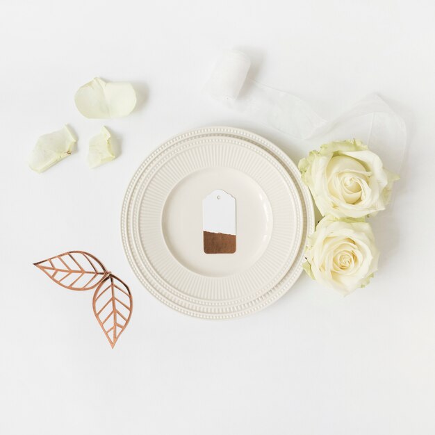 Blank tag on white plate with rose; leaves and ribbon on white background