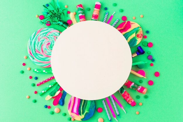 Blank white frame over party accessories and candies on green background