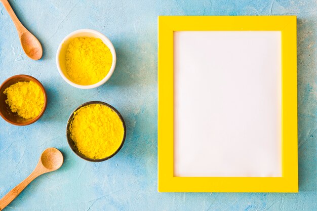 Blank white frame with yellow border near the holi color powder on concrete backdrop