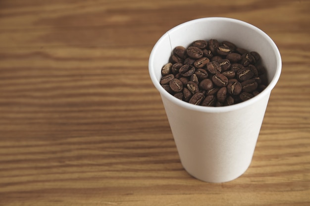 Blank white paper cup with good roasted coffee beans on thick wooden table in cafe shop