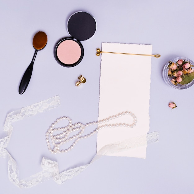 Free Photo blank white paper; dried pink rose bud in jar; ribbon; necklace; hairstick; oval brush; compact powder; golden hairpin and clutcher