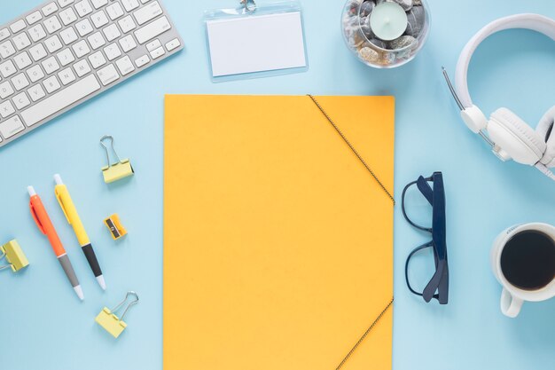 Blank yellow paper with candle; keyboard; headphone ; coffee cup and eyeglasses on blue backdrop