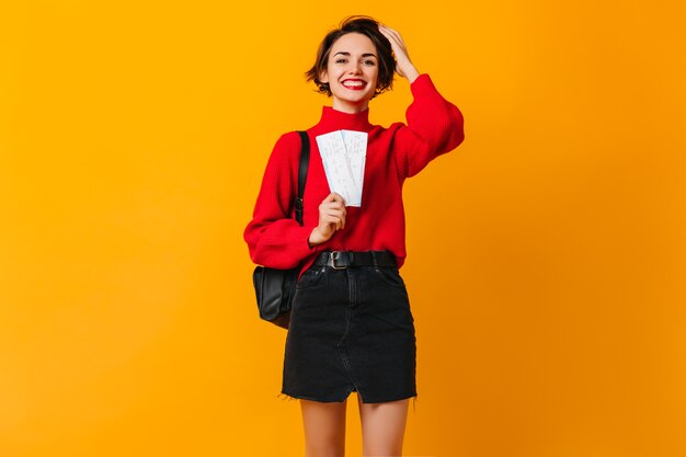 Blissful female tourist in red sweater holding tickets