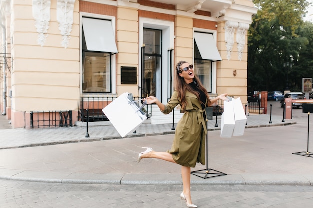 Free photo blissful shopaholic woman dancing on the street with smile