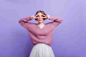 Free photo blissful young woman fooling around while posing in trendy purple sweater. graceful lady with dark-brown hair making funny faces during indoor photoshoot