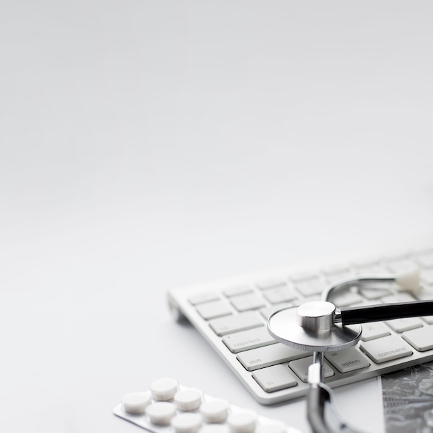 Blister pack of pills and stethoscope with wireless keyboard on white background