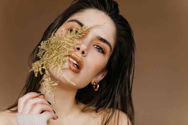 Free Photo blithesome european woman posing on brown wall with plant. close-up shot of carefree girl with green leaf.