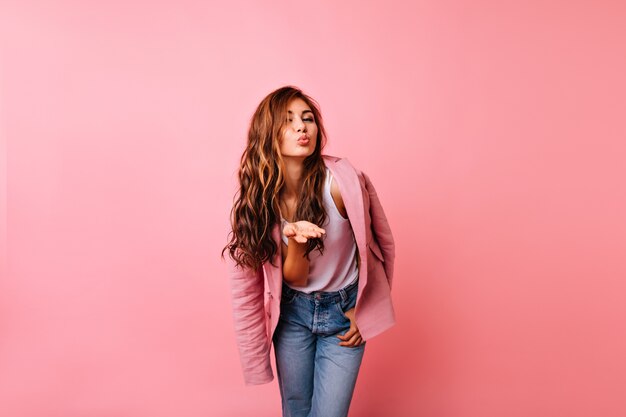 Blithesome girl in jeans posing with kissing face expression. Appealing red-haired lady sending air kiss.