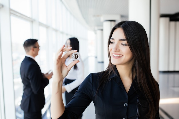 Blockchain and investment concept. Business woman leader holding bitcoin in front of his discussing team on office.