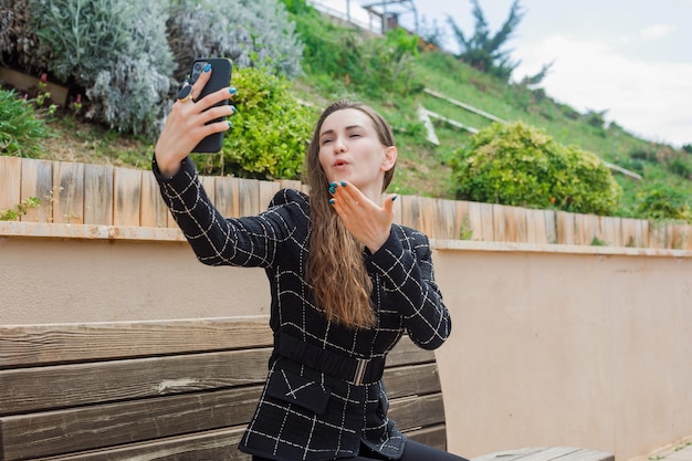 Blogger girl is taking selfie with her smartphone by blowing kiss in park