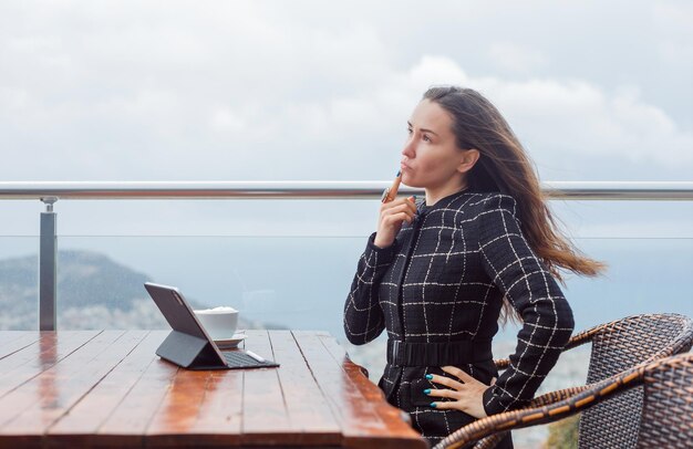 Blogger girl is thinking by holding forefinger on lips and putting other hand on waist by sitting on city view background