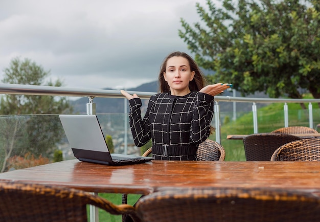 Blogger girl with laptop is looking at camera by sitting on nature view background