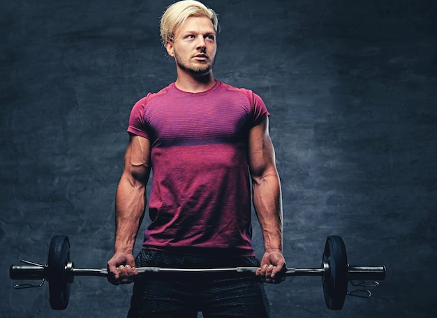 Free photo a blond, athletic male dressed in a red sportswear holds barbel.