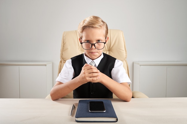 Blond Caucasian boy sitting in office and pretending to be executive