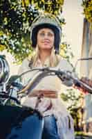 Free photo blond female in moto helmet sitting on moto scooter over green leafs and sun.