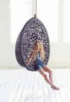 Free photo blond female teenager relaxing in round black artistic chair.