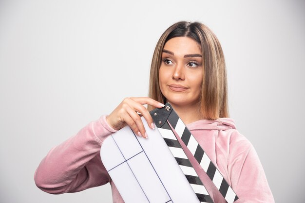 Blond lady in pink sweatshier holding a blank clapper board and gives natural poses