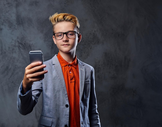 Free Photo blond teenager boy in a jacket and eyeglasses holds smartphone.