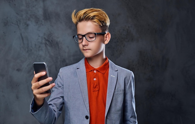 Free Photo blond teenager boy in a jacket and eyeglasses holds smartphone.