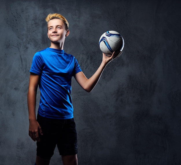 Free Photo blond teenager, soccer player dressed in a blue uniform holds a ball.