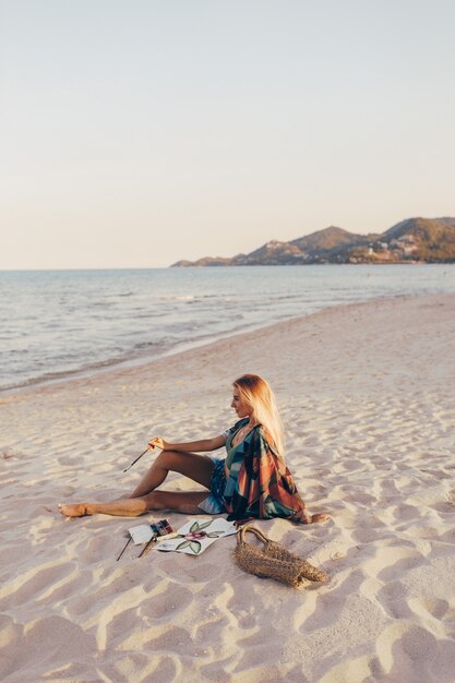 Blond woman drawing watercolor flower by brush on the beach