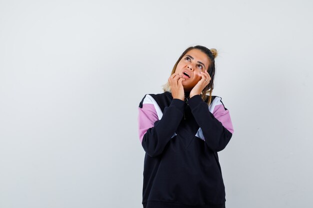 Blond woman holding hands on face, looking up in black tracksuit and looking wistful