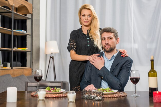 Blond woman hugging man at table with plates and glasses