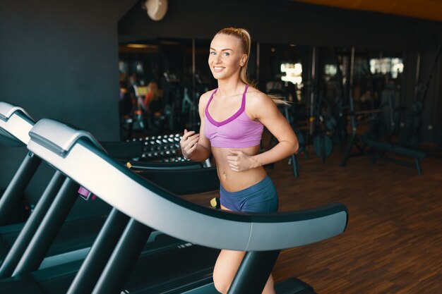 Blond young, motivated woman running on the treadmill