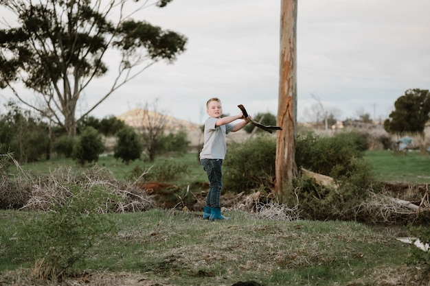 Blonde boy breaking a branch of a tree into two parts for firewood in nature