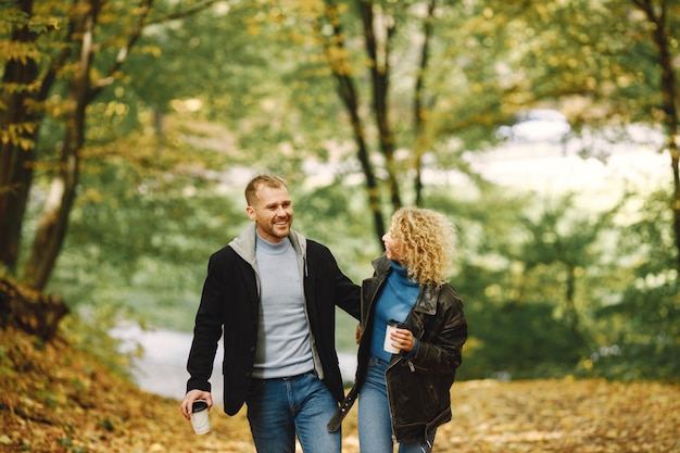 Blonde curly woman and man holding hands in autumn forest and hugging