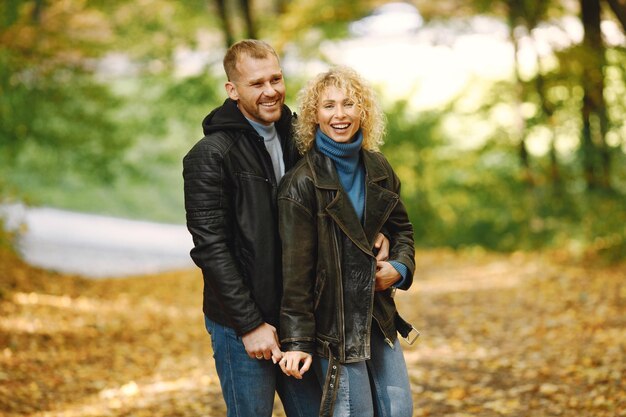 Blonde curly woman and man standing in autumn forest and hugging