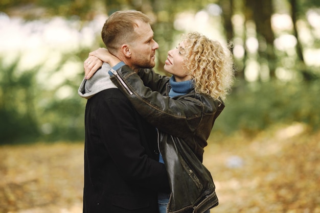 Free photo blonde curly woman and man standing in autumn forest and hugging