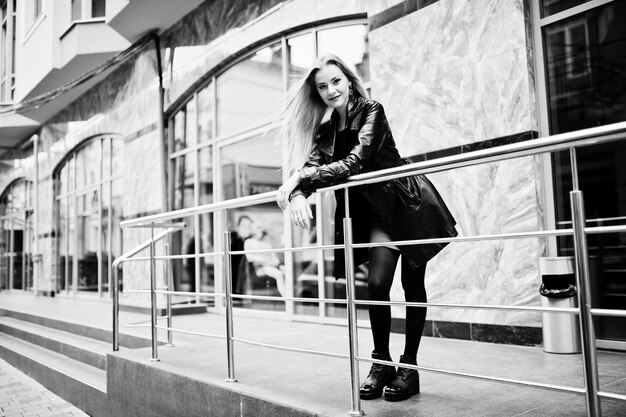 Blonde fashionable girl in long black leather coat posed at iron railing