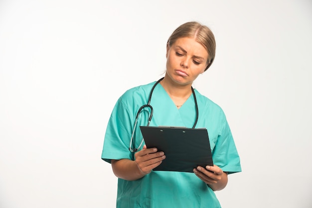 Blonde female doctor in blue uniform holding a receipt book and carefully checking it.