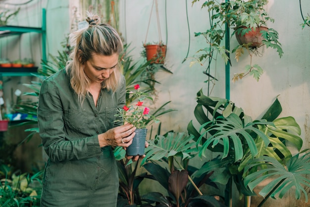 Free photo blonde female gardener taking care of flowering plants in the nursery