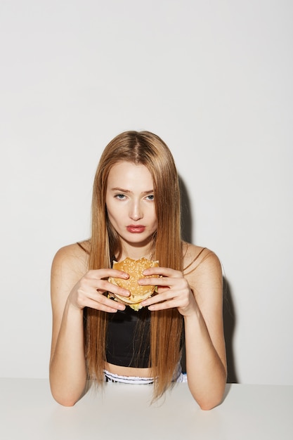 Free photo blonde female model with cheekbones and blonde hair holding burger with hands, with face expression.