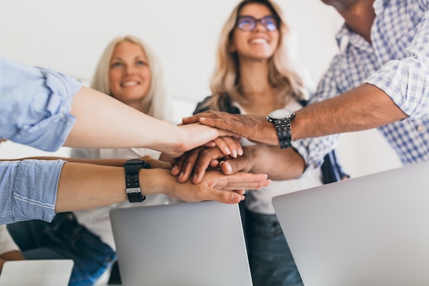 Free photo blonde female office worker looking up with smile while holding hands with colleagues. indoor portrait of friends ready to start joint work project.